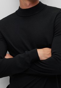 Czarny sweter z golfem, długimi rękawami, prążkowaną teksturą i dopasowanym krojem. Materiał wydaje się gładki i lekki.