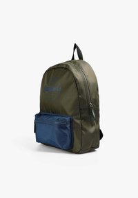 Mochila de nailon verde oliva con un bolsillo frontal con cremallera en azul marino, de forma redondeada y asas negras. Presenta un logo impreso en azul en la parte frontal.