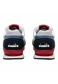 Sneaker bianche, navy e rosse con colletto imbottito, materiali in rete e suede, e un logo "diadora" ben visibile sul tallone.