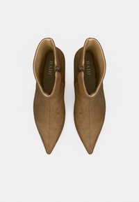 Bottes cheville en suédine marron avec bout pointu, détail de fermeture éclair latérale et texture lisse. La tige présente des accents de couture subtils.