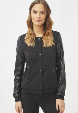 Cazadora bomber negra con un cuerpo de tejido texturizado y mangas de cuero brillante. Presenta botones a presión y bolsillos laterales.