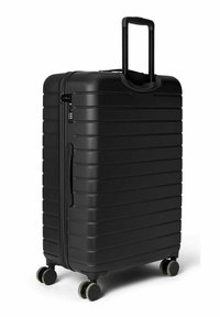 Valise rigide noire à surface striée, poignée télescopique et quatre roues. Comprend une poignée latérale et une serrure à combinaison pour la sécurité.