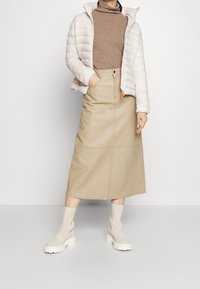 Puffer jacket in light gray, a fitted brown sweater, and a beige leather midi skirt paired with cream-colored ankle boots. Simple design.