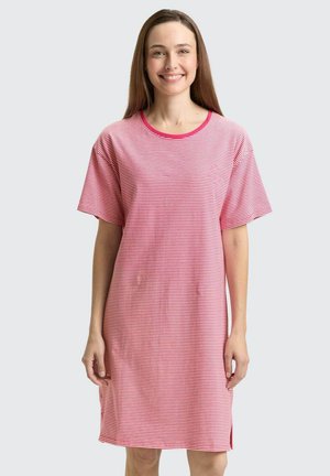 Lachende vrouw met lang bruin haar, die een losse roze en wit gestreepte T-shirtjurk tot op de knie draagt met korte mouwen.