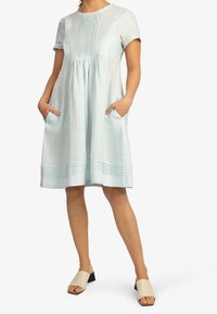 Jasnoniebieska lniana sukienka z krótkimi rękawami, plisowanym przodem, luźnym fasonem, bocznymi kieszeniami oraz dołem z poziomym detalem szycia.