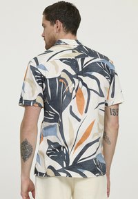 Chemise à manches courtes en tissu léger, arborant un imprimé botanique multicolore dans des tons marine, beige, orange et bleu.