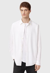 Camisa blanca de manga larga hecha de algodón, con cuello abotonado, bordado sutil en el pecho y un corte relajado.