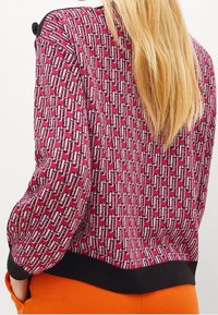 Gebreide sweatshirt in het roze met een geometrisch patroon; heeft een zwarte geribbelde zoom en schouderaccenten. Zachte textuur en een ontspannen pasvorm.