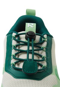 Lekkie buty sportowe w kremowym kolorze z zielonymi akcentami. Posiadają siateczkową cholewkę, elastyczne sznurówki oraz zapięcie na toggle dla zapewnienia pewnego dopasowania.