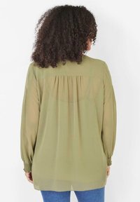 Olivově zelená, lehká halenka s dlouhými rukávy a nařasenými manžetami. Má záhybový detail na zadní straně a volný střih.