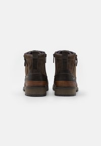 Bottes en cuir marron avec des accents marron contrastants, des zips latéraux et une doublure texturée à motifs. Semelle en caoutchouc épaisse avec des crampons visibles.