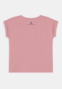 Różowy t-shirt z krótkim rękawem z okrągłym dekoltem i małym logo "Calvin Klein Jeans" nadrukowanym na plecach w pobliżu linii szyi. Miękka w dotyku.