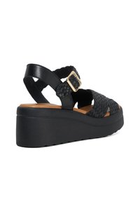 Zwarte plateau-sandalen met geweven leren crisscross banden en een gouden gespaccent. Voorzien van een gevoerde tan binnenzool en een gestructureerde zwarte buitenzool.