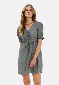 Čierne a biele kárované šaty s puzdrovými rukávmi, výstrihom do V a stiahnutým pásom. Obsahujú uzáver na viazanie a rozšírenú sukňu.