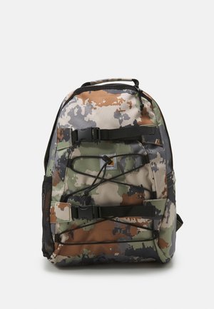 Sac à dos camouflage avec sangles à boucles à l'avant, cordons élastiques, poche latérale en maille et poignée supérieure sur un fond uni.