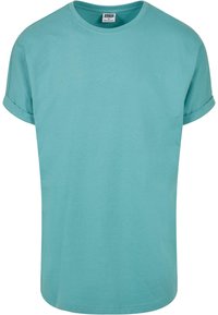 Camiseta de manga corta turquesa con cuello redondo, hecha de algodón suave, que presenta un corte holgado y mangas enrolladas para un detalle adicional.
