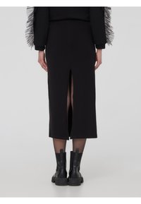 Gonna midi nera con spacco posteriore, realizzata in tessuto liscio. Abbinata a stivaletti neri alla caviglia. Il modello è mostrato di spalle.