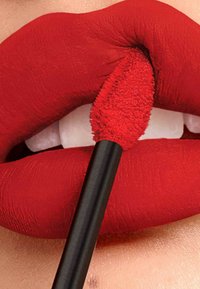 Un rouge à lèvres liquide rouge est appliqué avec un applicateur à embout flou sur des lèvres lisses et pulpeuses. Les lèvres présentent une finition mate vibrante et une forme définie.