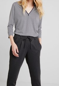 Zwart-wit geblokt langemouwen top met een V-hals, gecombineerd met donkergrijze geblokte broek met zijzakken en een trekkoord in de taille.