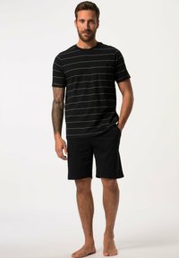 Camiseta de rayas negras con finas líneas blancas y mangas cortas, combinada con pantalones cortos negros. Tejido de algodón casual, sin logotipos o patrones visibles.