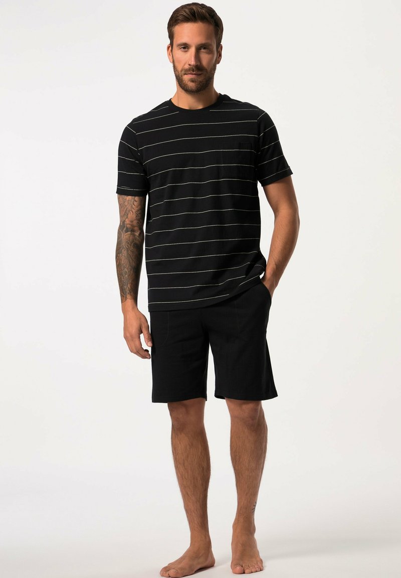 Camiseta de rayas negras con finas líneas blancas y mangas cortas, combinada con pantalones cortos negros. Tejido de algodón casual, sin logotipos o patrones visibles.