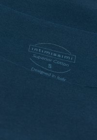 Marinblått bomullstyg med en slät textur. Har en tryckt etikett som anger varumärke, material, storlek (S) och designursprung i Italien.