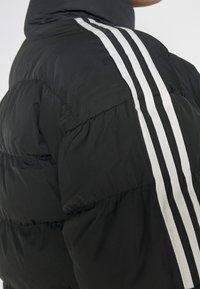 Black puffer jacket with white three-stripe detail running from shoulder to back, worn by a person turned away from the camera.