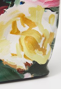 Primo piano di una borsa in pelle texture con stampa floreale astratta in tonalità gialle, bianche, verdi e rosa e piccolo logo metallico di Ted Baker London.