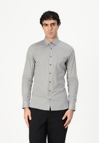 Camicia button-up in un tessuto grigio chiaro con un motivo geometrico in blu navy e azzurro, dotata di colletto alla francese e maniche lunghe.