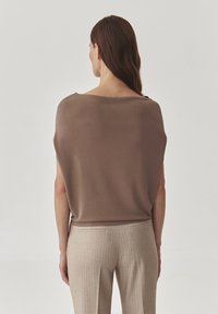 Hnědý volný top vyrobený z lehkého materiálu, s širokým výstřihem. V kombinaci se světle béžovými pruhovanými kalhotami, které mají střih na míru.