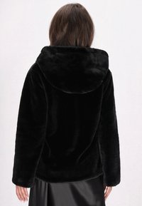 Sort faux fur jakke, oversized design, hætte med glat tekstur. Lange ærmer og lige kant. Subtil glans på materialet.