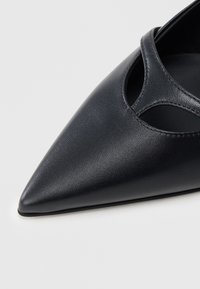 Μαύρο δερμάτινο παπούτσι με μυτερή μύτη και σχεδιασμό με ανοίγματα στα πλαϊνά, με λεία υφή. Η σόλα είναι επίπεδη με μινιμαλιστικό προφίλ.