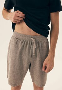 Szare bawełniane szorty z elastycznym paskiem i sznurkiem, o luźnym kroju i miękkiej fakturze, zestawione z czarną koszulą.
