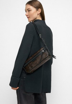 Woman wearing black knit sweater and dark pants, carrying dark brown rectangular leather crossbody bag over shoulder.