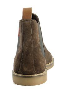 Stivaletto in suede marrone con pannelli laterali elastici, una linguetta in pelle tan e una suola in gomma con un design cucito sulla suola.