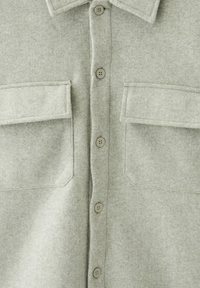 Veste-chemise en laine gris clair avec boutons sur le devant, deux poches à rabat sur la poitrine et un col pointu.