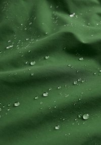 Zelená voděodolná látka s hladkým povrchem, na níž se nacházejí rozptýlené kapky vody, které zdůrazňují její vodoodpudivé vlastnosti.