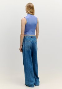 Lichtpaarse geribde crop top gecombineerd met wijde blauwe denim jeans, met een hoge taille en achterzakken, gezien vanuit de achterkant.