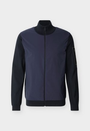 Navy blue and black zip-up jacket with high collar, long sleeves, ribbed cuffs, and a small zip pocket on the left sleeve.