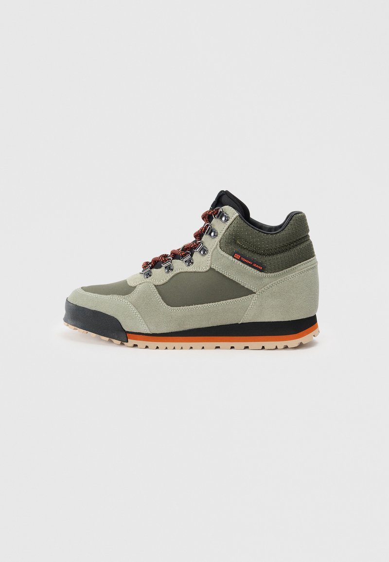 Grüne Wildleder-Wanderschuhe mit schwarzen Akzenten, orangefarbenen Details an der Sohle und mehrfarbigen Schnürsenkeln. Mittlere Schnittform für Knöchelsupport.