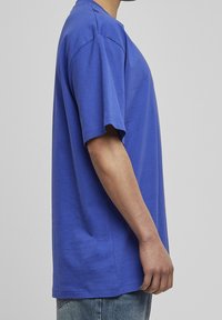 Królewsko-niebieska koszulka z krótkim rękawem, wykonana z miękkiej bawełny, z luźnym krojem i okrągłym dekoltem, zaprezentowana w profilu bocznym.