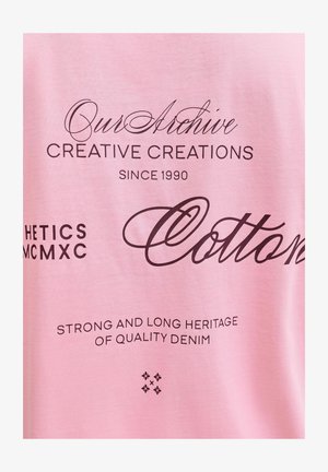 Maglietta di cotone rosa con testo stampato nero, inclusi "Our Archive", "Creative Creations" e "Quality Denim" in vari caratteri.