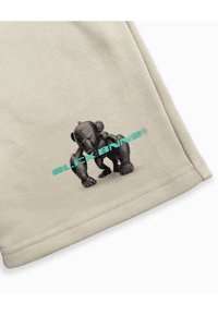 Beige shorts van zachte stof, met een zwarte grafische afbeelding van een humanoïde figuur en turkooizen tekst "BLCK BNNS".