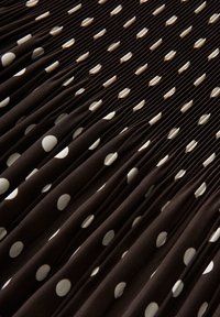 Black fabric with white polka dots features evenly spaced pleats creating a textured, repeating pattern.