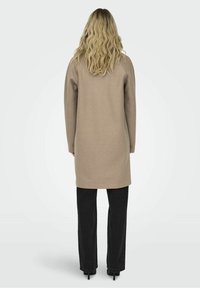 Suéter beige hasta la rodilla con mangas largas y un corte relajado, combinado con pantalones negros de corte holgado. Textura simple y suave.