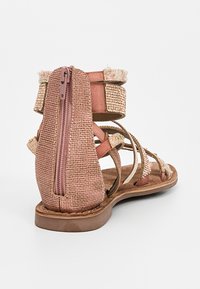 Różowe sandały gladiatorki z zamkiem z tyłu, o fakturowanej powierzchni, z wieloma paskami i ozdobnym paskiem na kostkę, płaską podeszwą oraz otwartym przodem na białym tle.