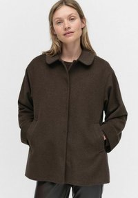 Bruine, gestructureerde jas met een kraag, lange mouwen en zijzakken. Minimalistisch ontwerp geschikt om over outfits te lagen.