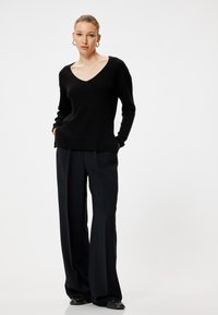 Zwarte gebreide trui met een diepe V-hals, gecombineerd met hoge taille, brede zwarte broek. Glad textuur, minimalistisch design, geen zichtbare patronen.
