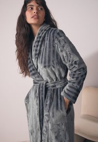 Grijze gestreepte badjas van pluche met een omslagkraag, een gebonden ceintuur en zijzakken. Zachte textuur en subtiele glans versterken het ontwerp.