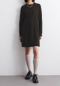 Robe longue à manches longues vert foncé avec une coupe droite, fentes latérales, associée à des chaussettes tricotées gris clair montant jusqu'aux genoux et des chaussures plateformes noires.